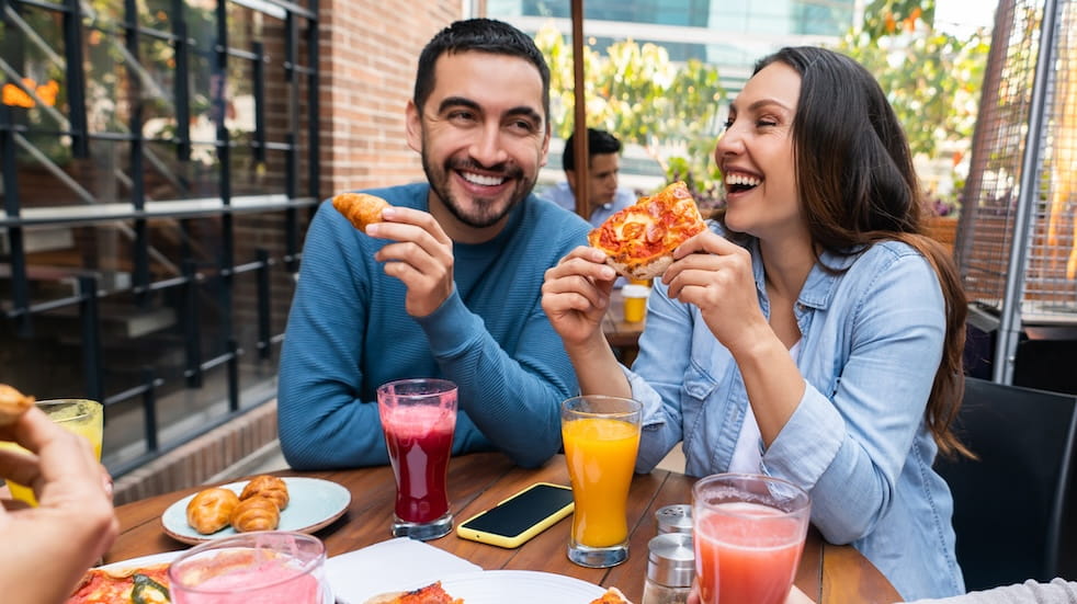 Happy couple having fun eating pizza at a restaurant with a group of friends and laughing
